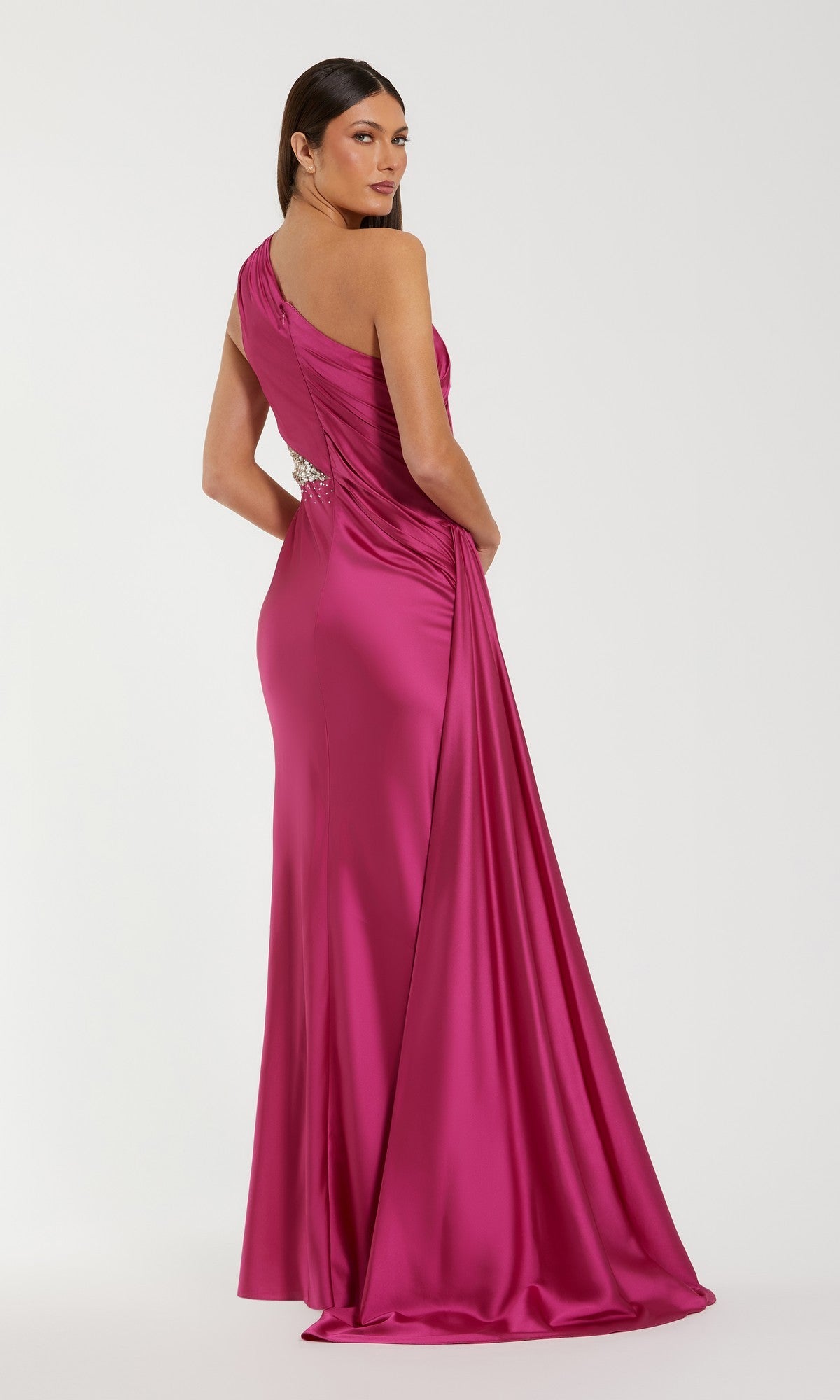 A woman models the Mac Duggal 2210 Cut-Out One-Shoulder Formal Dress, a floor-length magenta satin gown with a fitted silhouette, shown from a slight angle against a plain light background.